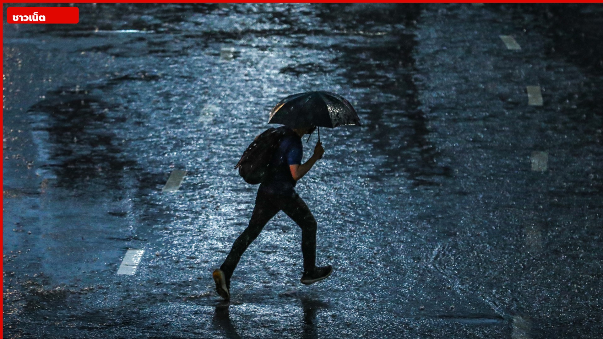 คนถือร่มเดินข้ามถนนเปียกในคืนฝนตกหนัก